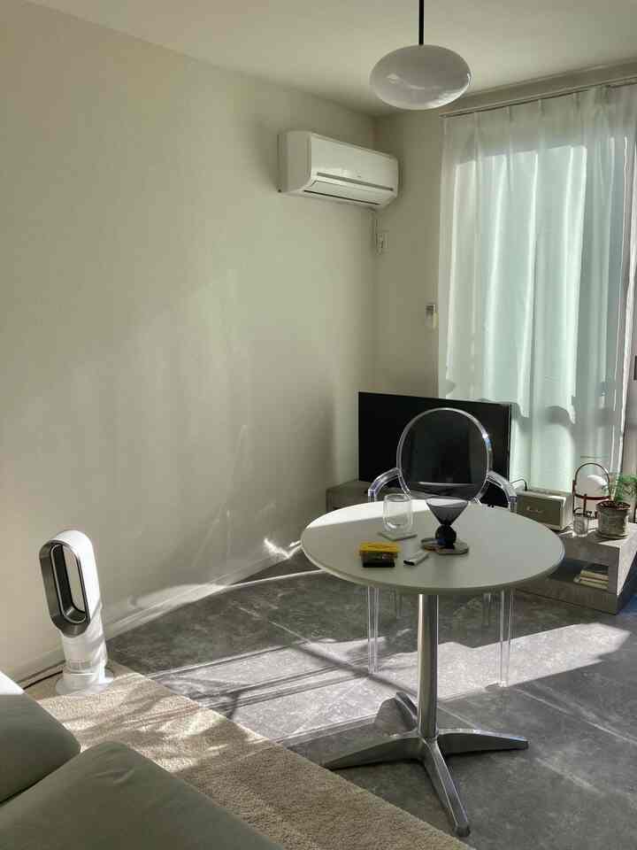 白とグレーのトーンの1LDKリビング、透明な椅子と円形テーブルが配置されたシンプルでモノトーンな空間