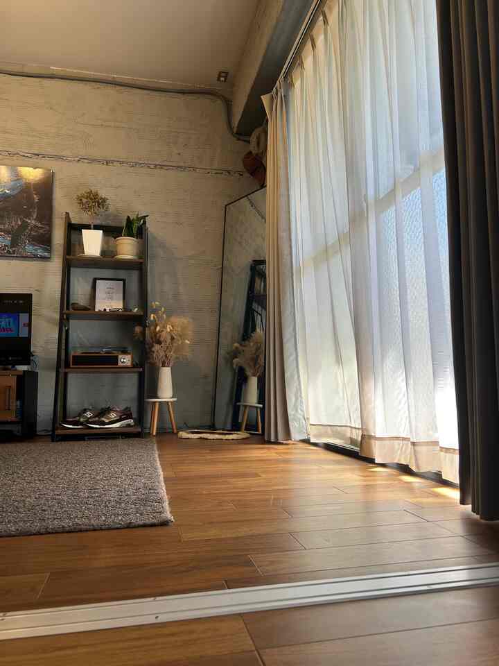 Natural wood-tone living room featuring a black open shelf, large mirror, and curtains in a cozy Nordic style interior