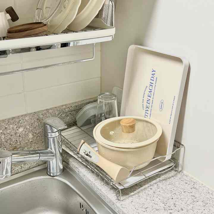 ベージュ色の鍋とトレイが置かれた食器乾燥ラックが設置された清潔なキッチンシンクスペース