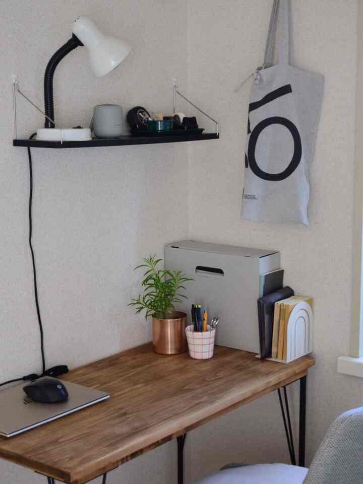 A small home office with white and wood tones featuring a desk, shelf, and organized stationery in a simple workspace