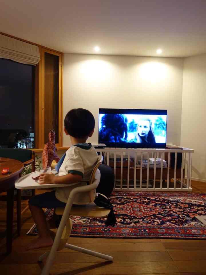 Wood tone and red-colored living room with a child sitting in a high chair watching TV, creating a cozy atmosphere