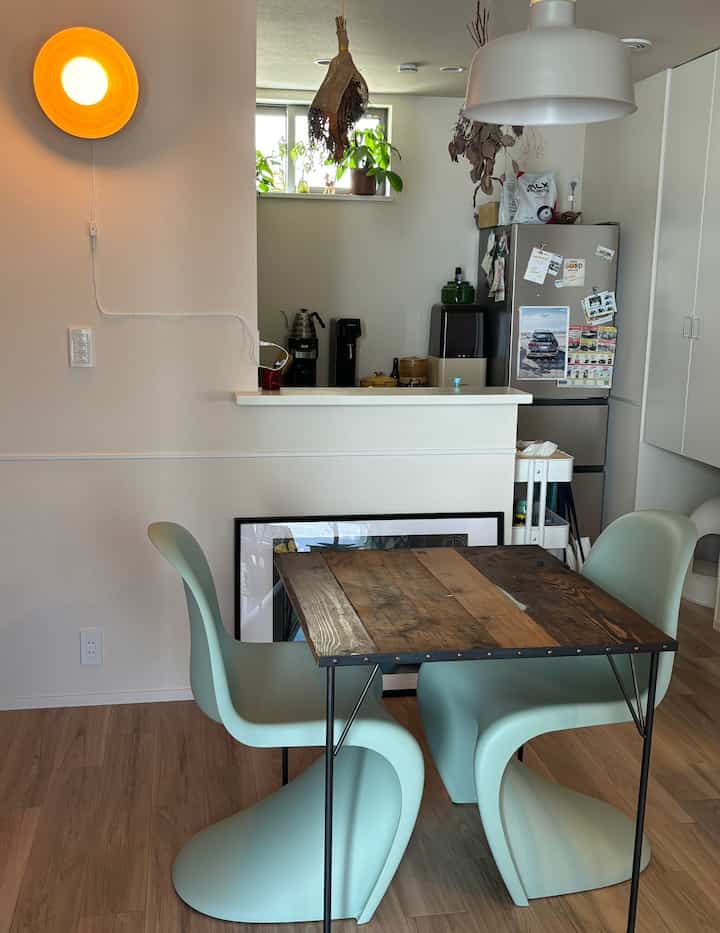 ウッド調テーブルとミント色のパントンチェアが配置されたナチュラルモダンなキッチンスペース、間接照明と植物が雰囲気を演出