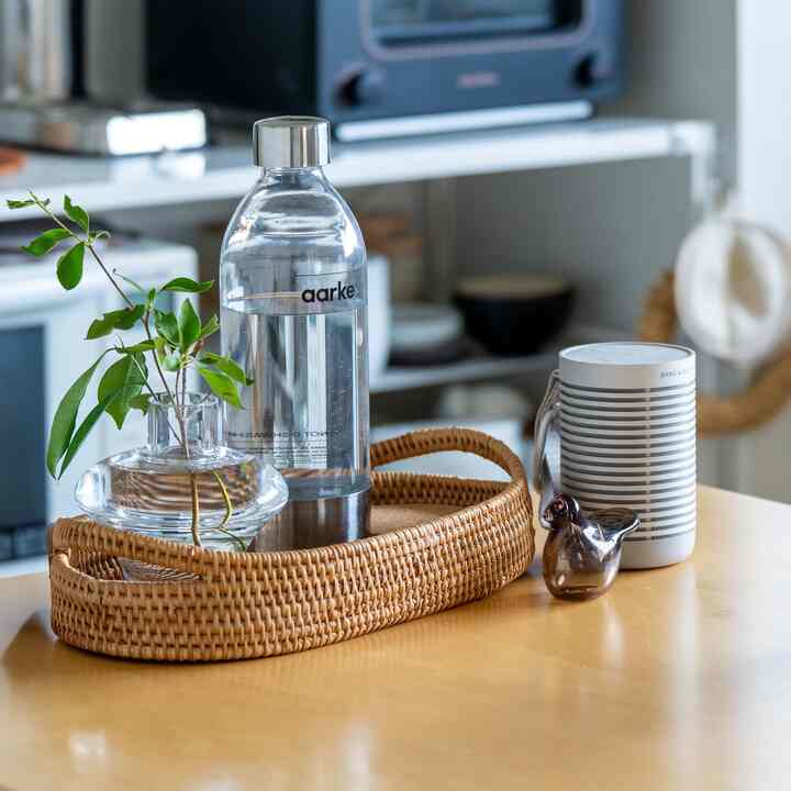 ナチュラルな木目調のダイニングテーブルにラタンのトレイ、透明な容器、ワイヤレススピーカーが置かれた整った空間