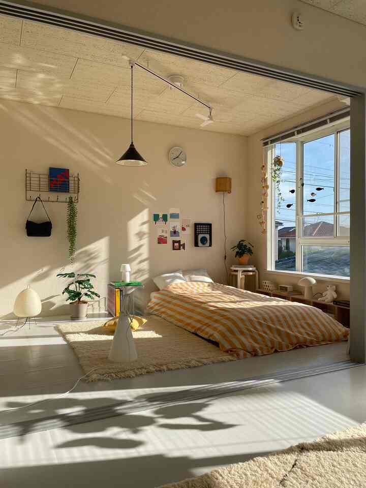 明るくナチュラルな色調の寝室、窓際にベッドと壁の装飾、たっぷりの自然光が差し込む空間