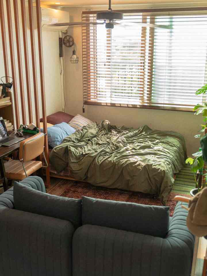 ナチュラルカラーの寝室とリビング、窓の木製ブラインド、ソファ、快適なベッドが配置された雰囲気のあるインテリア