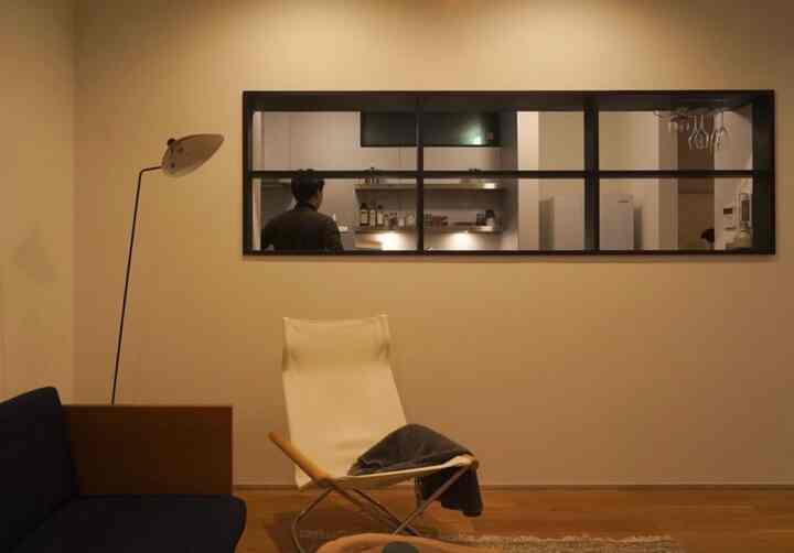 ブラウンの木目調床と白い壁にラウンジチェアとフロアランプが配置されたシンプルモダンなリビングとキッチンがつながる雰囲気のあるインテリア