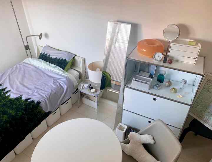 White and gray toned studio bedroom featuring a bed and round table in a clean, modern space