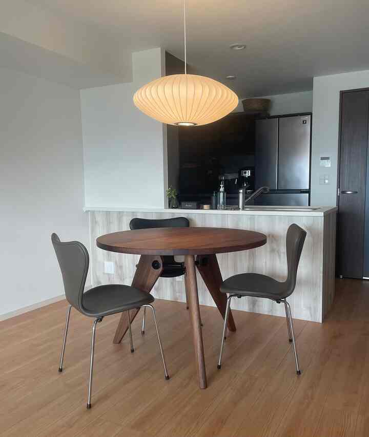 木目調の床と丸い木製ダイニングテーブル、ネイビーの椅子が2脚あるシンプルモダンなダイニングルームとキッチンのインテリア