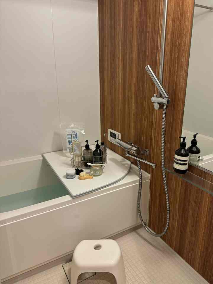 A clean bathroom featuring white and wood tones, with a bathtub, shower, and a small stool arranged neatly