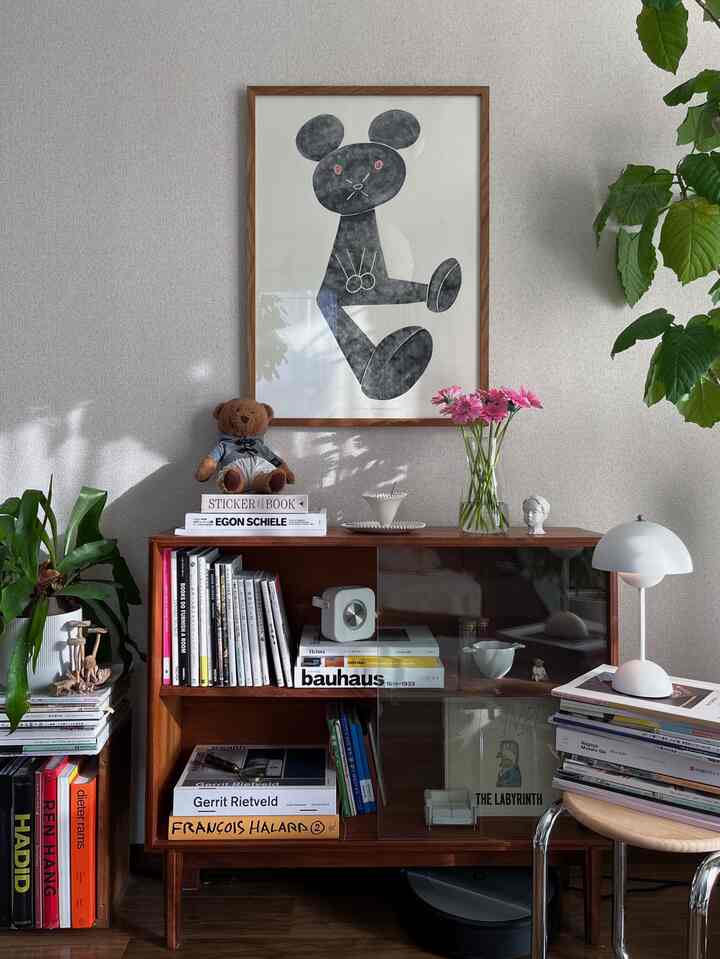 Natural-toned living room featuring a wooden bookshelf, a stuffed bear, and green plants with a cozy atmosphere