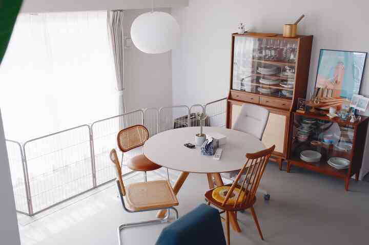 Gray and natural-toned dining room featuring a round table, assorted chairs, and a dog gate with a crate, creating a cozy pet-friendly atmosphere