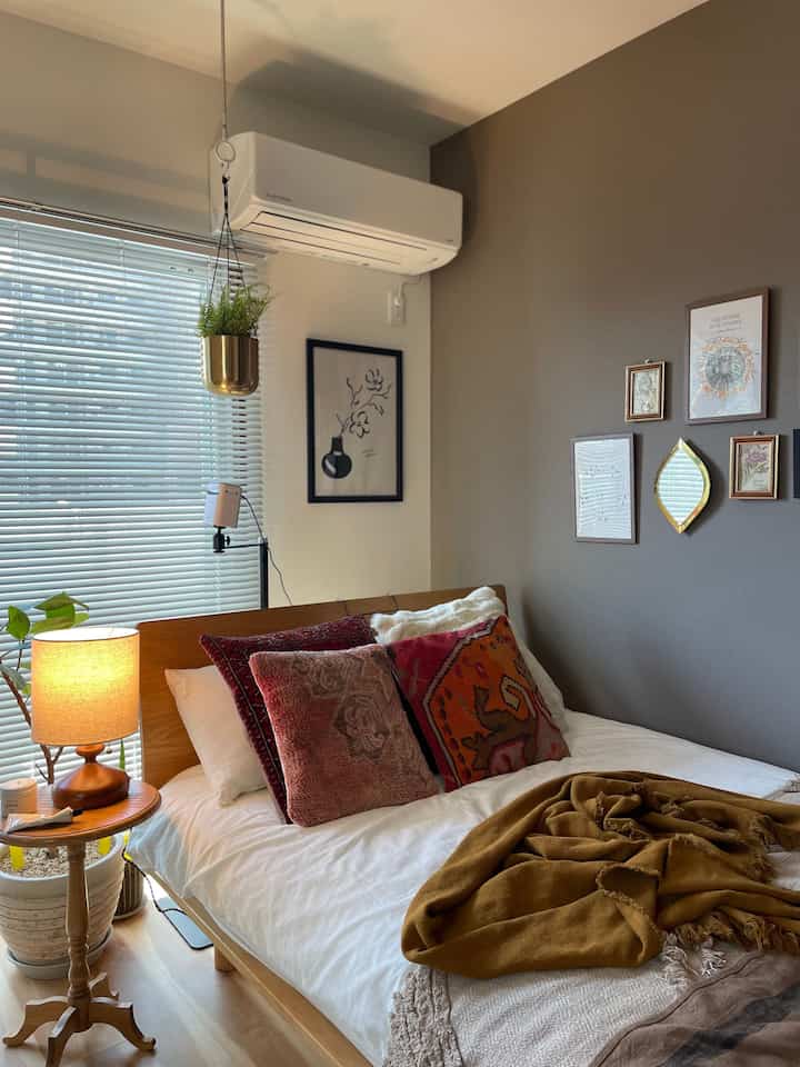 暖かい木目調と赤のアクセントが調和する寝室、ベッドサイドテーブルとヴィンテージクッションが配置された雰囲気のあるレトロな空間