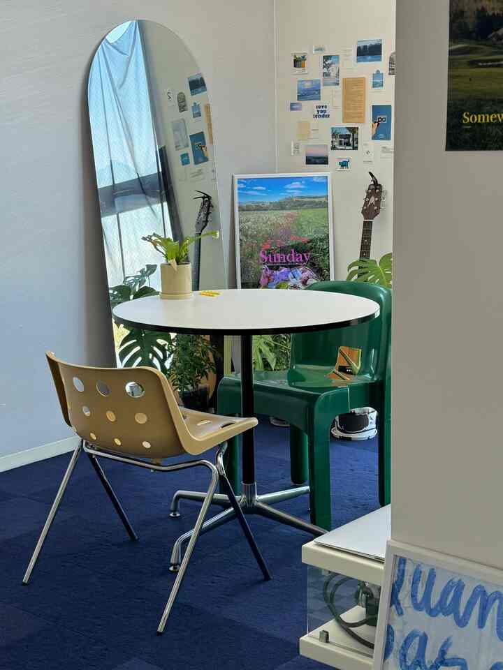 青いタイルカーペットの床、白い丸テーブルと二脚の椅子、植物が配置されたワンルームのカフェ風で印象的なインテリア