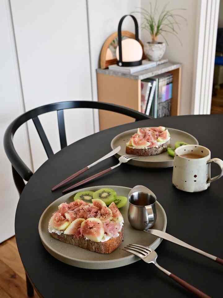 Black table with brown furniture in a dining space, featuring fig toast and coffee set in a cozy cafe-style interior