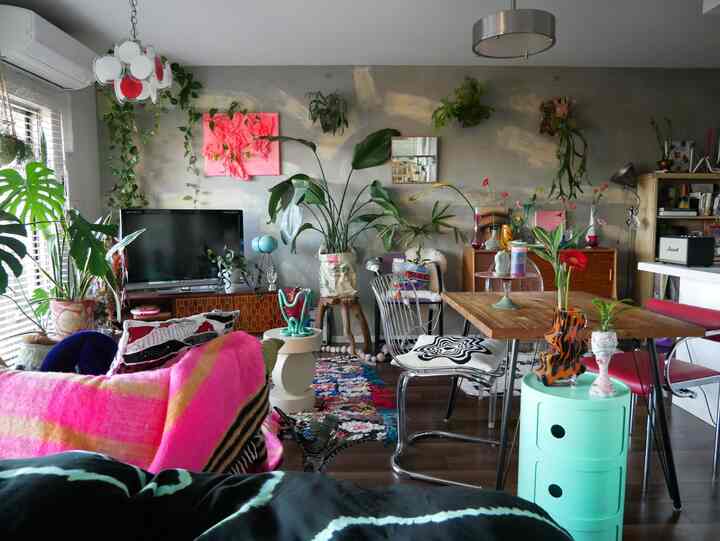 ナチュラルな色調のリビング兼ダイニングルーム、多数の植物と鮮やかなピンクのソファが配置された、印象的で心地よい空間