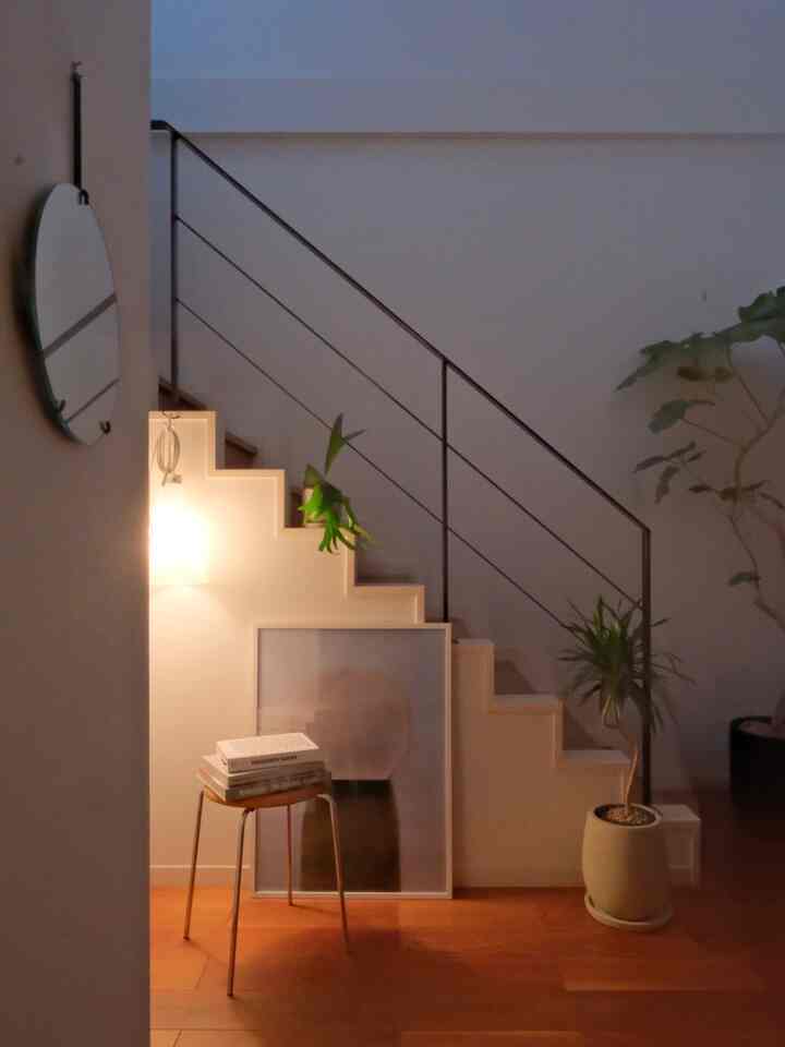 木目調の床とコーナー収納階段、植物、スツール、ポスターが配された落ち着いたミニマルな廊下のインテリア