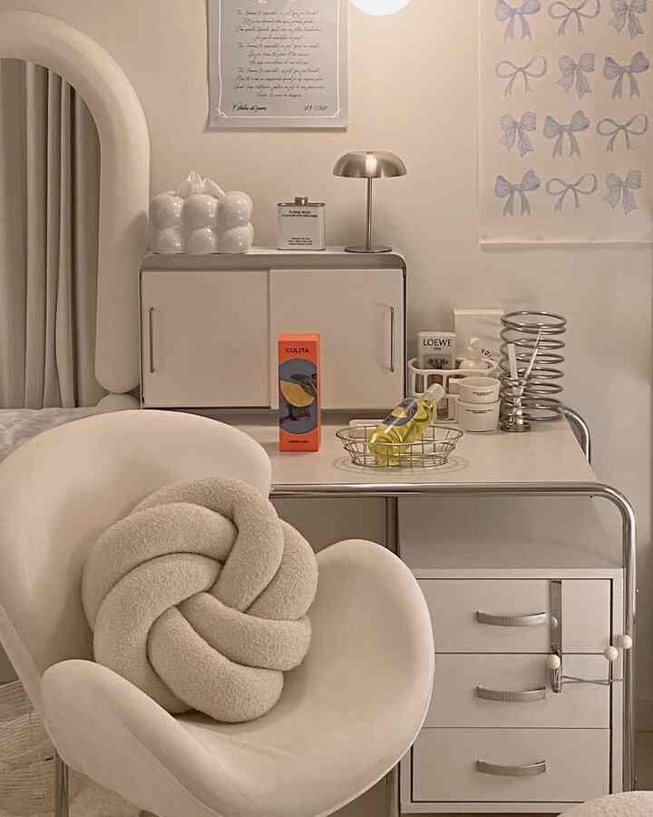 ナチュラルカラーのリビング、アイボリーのアームチェアと結びクッション、ミニマルなデスクとディフューザーが配置されたシンプルなインテリア