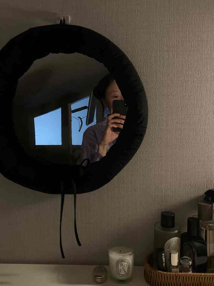 黒いクッションフレームの鏡と白い壁が特徴的な寝室のドレッサー、キャンドルと香水が静かな雰囲気を演出