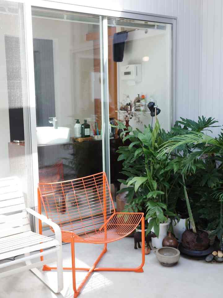 Bright courtyard space in white and natural tones featuring orange metal chair and lush plants with a clean, minimal atmosphere