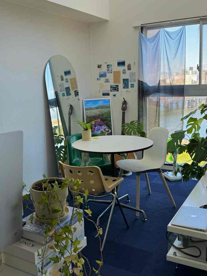 ダークブルーのカーペットと複数の植物が配置されたワンルームのリビング、中央に丸いダイニングテーブルと様々な椅子があるミニマルな空間