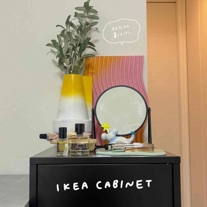 Black IKEA cabinet topped with yellow vase, round mirror, and perfumes creating cozy workspace interior