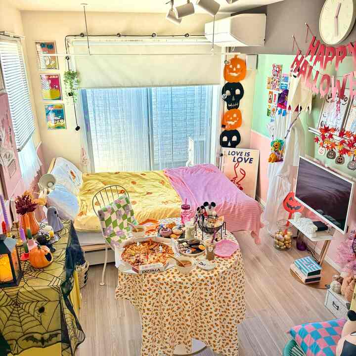 暖かいイエローとピンクのトーンが調和した一人暮らしの寝室兼リビング、ハロウィンデコとホームパーティーのセットアップが印象的な空間