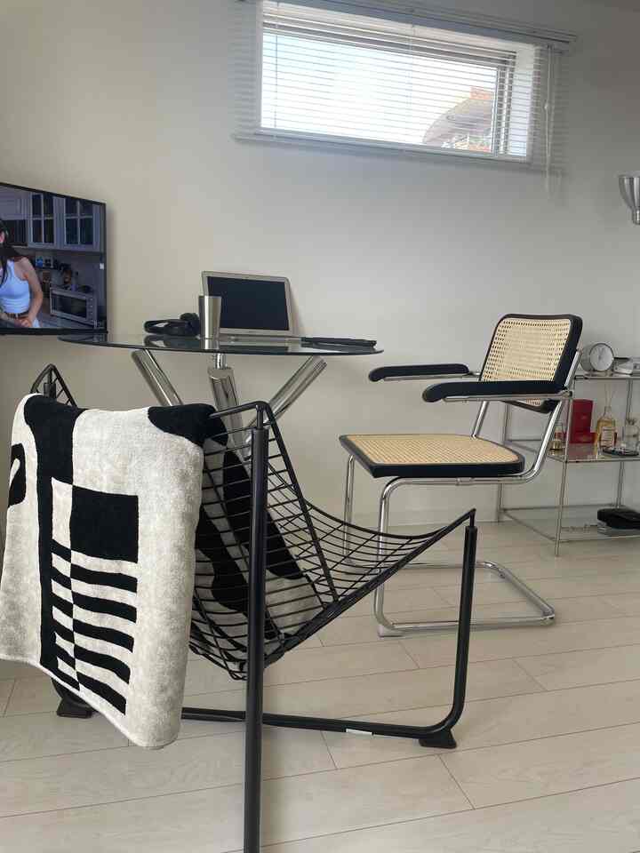 White-toned living room and home office space featuring a glass table, rattan armchair, and black metal frame chair for a clean interior