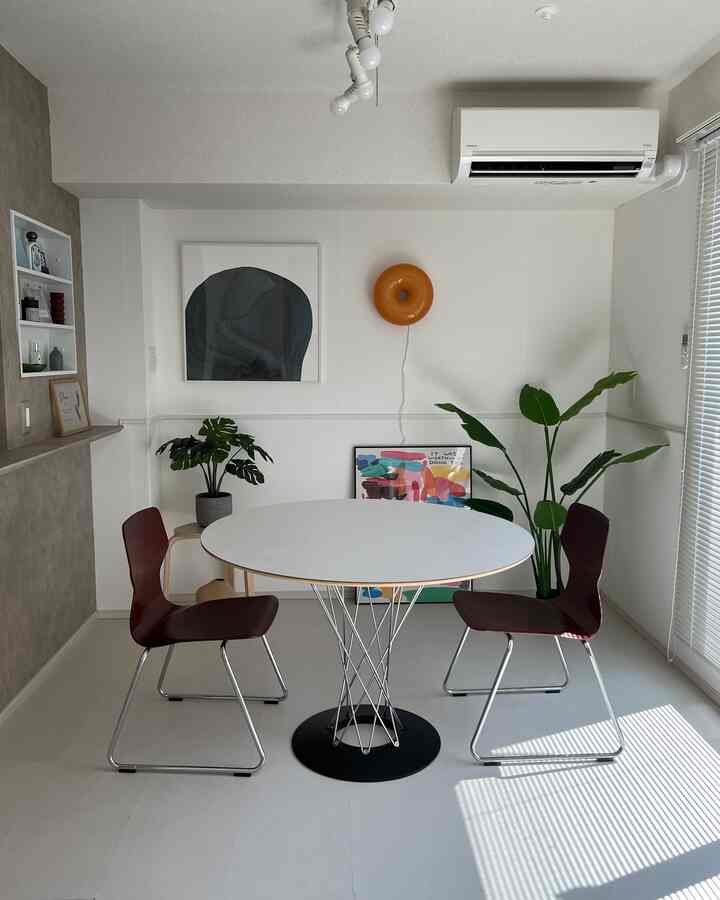 ホワイトトーンのダイニングルーム、丸いダイニングテーブルと茶色の椅子2脚が配置されたモダンでナチュラルな空間