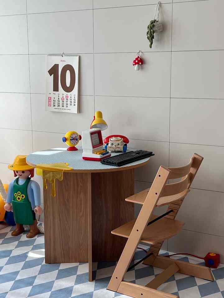 木目調と白を基調とした子供スペース兼リビング、丸テーブルの上におもちゃと黄色いランプが置かれた雰囲気のあるインテリア