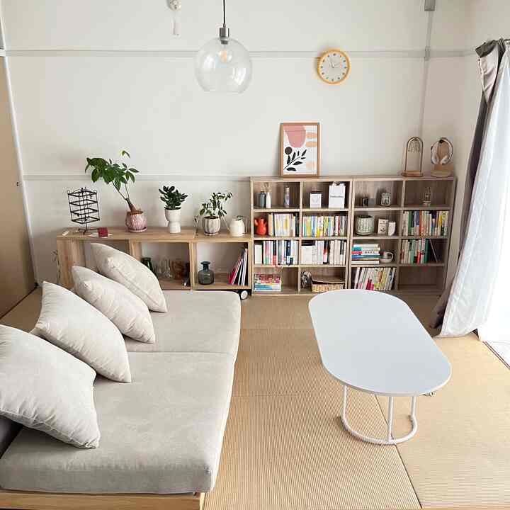 明るいナチュラルトーンのリビング、ベージュのソファと白のコーヒーテーブル、木製の本棚が配置されたすっきりとして広々とした空間