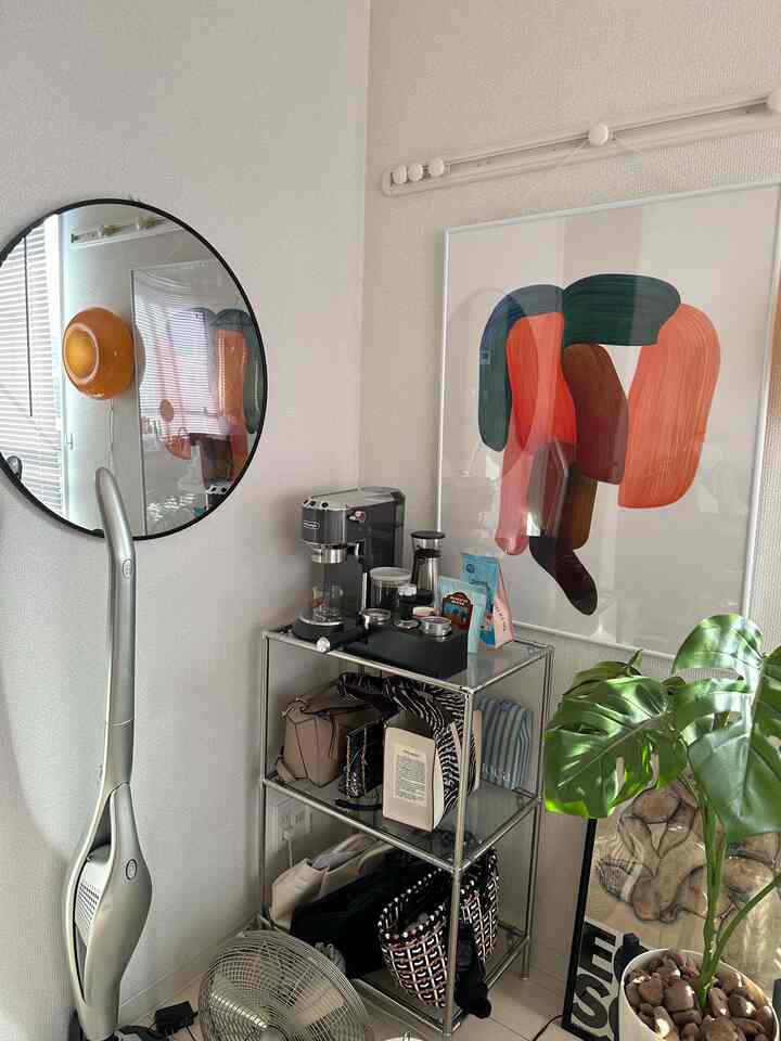 A modern home cafe in a white and silver toned compact room featuring a coffee machine, metal storage rack, large green plant, and round wall mirror