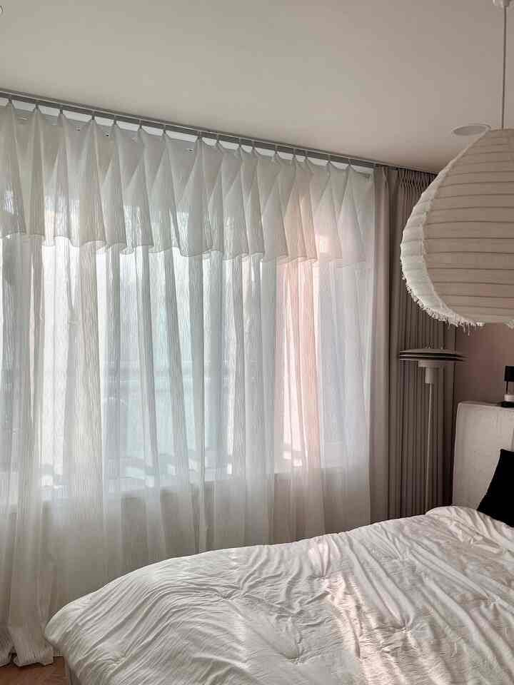 柔らかなベージュとホワイトの色調の寝室、重ねたシアーカーテンと快適なベッドが配置された自然な雰囲気のインテリア