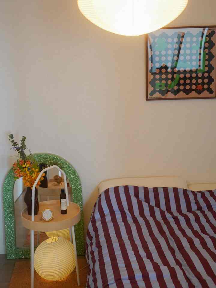 ナチュラルな色調の寝室で、ストライプ柄の掛け布団カバーと緑色の鏡が配置された雰囲気のあるインテリア