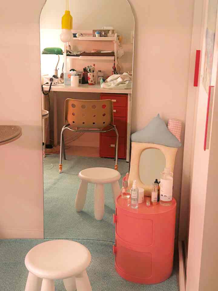 ピンクと白を基調とした狭い部屋にミニマルな化粧台とスツール、印象的なアーチ形の鏡が配置された雰囲気のあるインテリア