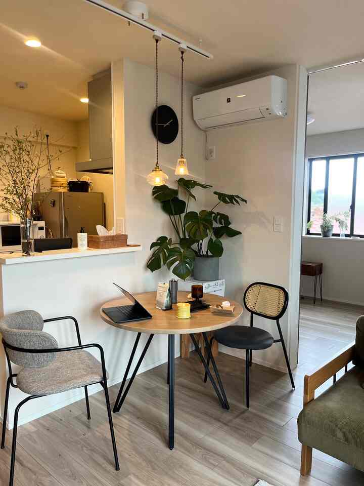 Modern dining room with natural wood tones and white walls, featuring a round dining table, pendant lights, and greenery