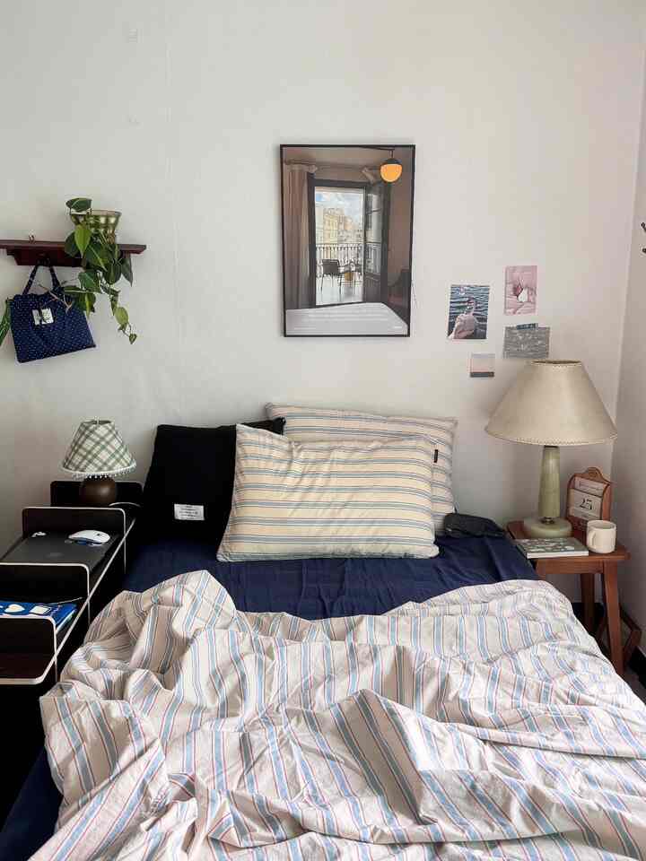 白い壁とネイビーとベージュの寝具がある寝室、中央に配置されたベッドとナイトテーブルがあるシンプルなインテリア