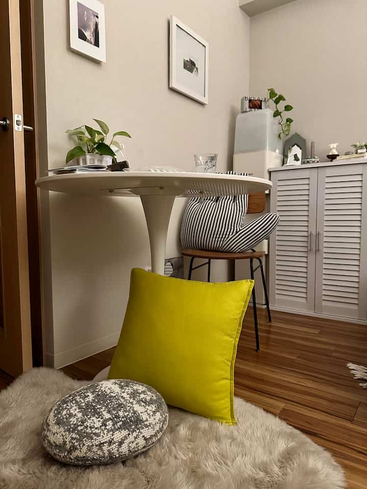 ナチュラルな色調のダイニングルーム、白い円形テーブルと木製椅子、黄色とグレーのクッションが置かれた温かみのあるラグのある印象的な空間