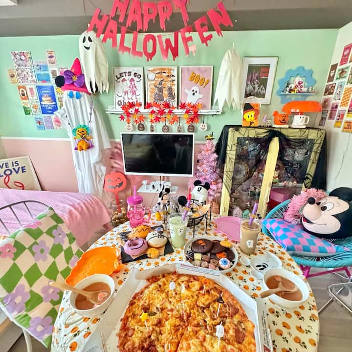 ピンクとホワイトの色調のリビングルーム、ハロウィンの飾りと食べ物が置かれたテーブルが華やかなホームパーティーの雰囲気を演出するインテリア