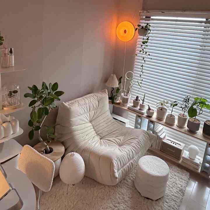 A cozy living room in warm beige and white tones featuring a plush sofa, stool, and numerous plants in a natural modern style