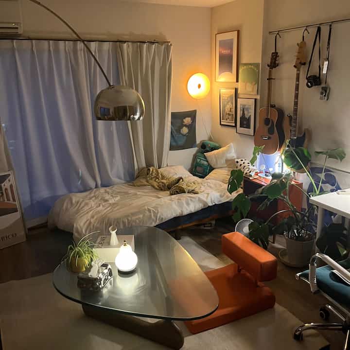 Warm-toned natural wood 8-tatami room featuring bed, Noguchi coffee table, houseplants, and guitars in cozy single household space