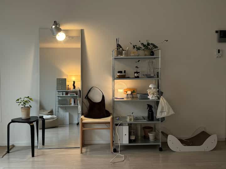 シルバーの棚、大きな全身鏡、木製スツールが配置されたミニマルで落ち着いたリビング空間