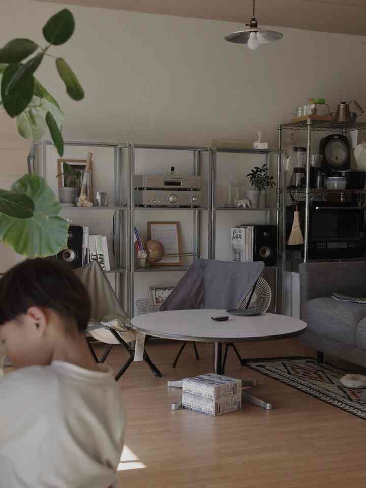 ナチュラルカラーのリビング、グレーのソファと丸いコーヒーテーブル、メタルシェルフが配置された落ち着いた雰囲気のインテリア