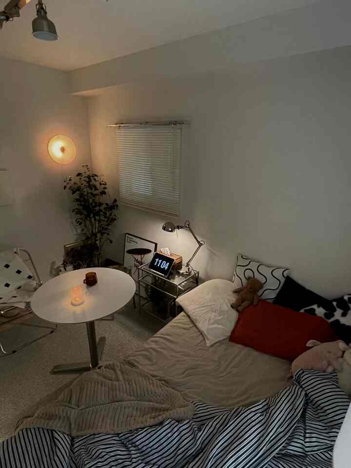 ナチュラルな色調のワンルーム寝室、シルバーのスツールとテーブルランプが配置された落ち着いた雰囲気のあるインテリア