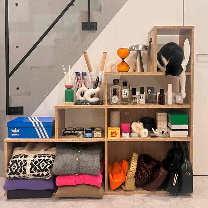 Natural-toned interior featuring a wooden shelf neatly organized with clothes and items next to concrete stairs, with a cat perched on top.