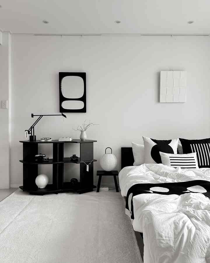 モノトーンの黒と白のシンプルな寝室、黒いベッドと棚、白いクッションと寝具が配置された雰囲気のあるインテリア