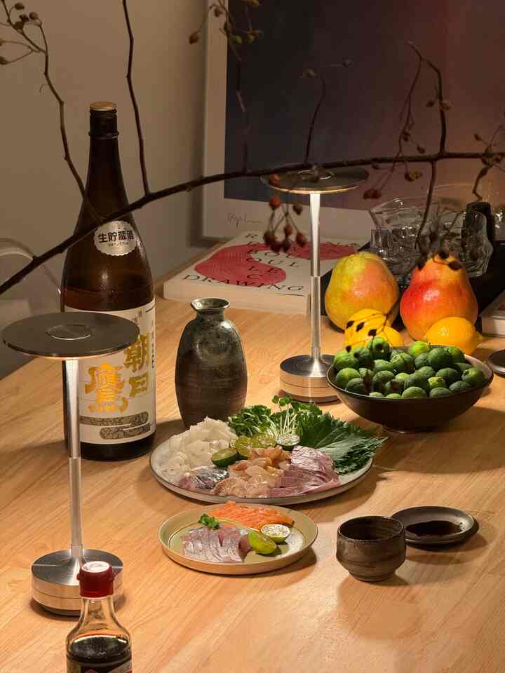 木目調のダイニングテーブルに刺身皿と酒瓶、果物が配置された雰囲気のあるホームパーティースペース