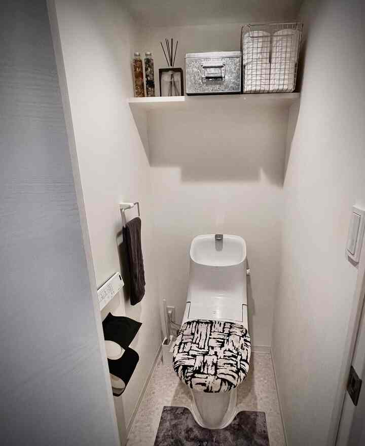 白を基調としたコンパクトなワンルームのトイレ、モダンな便器とパターンの便座カバーが整った空間