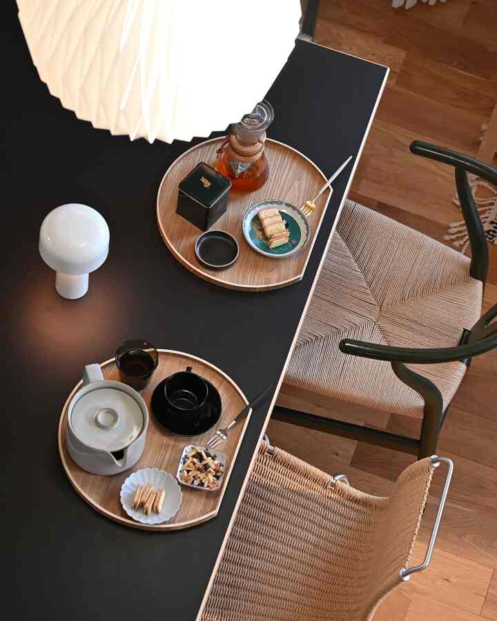 Nordic dining space featuring wood tones and black tabletop, cozy snack time setup with half-moon trays holding tea and cookies