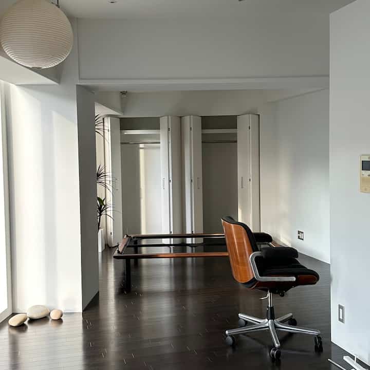 Natural studio bedroom with white walls and wood-tone flooring, featuring a pendant light and a storage closet, creating a calm atmosphere