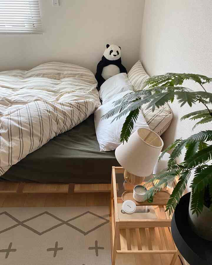 ナチュラルな木目調と白を基調とした寝室に、サイドテーブルとパンダのぬいぐるみ、植物が配置された雰囲気のあるインテリア